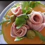 Coppa di melone con rose di prosciutto cotto, olive verdi e rucola.